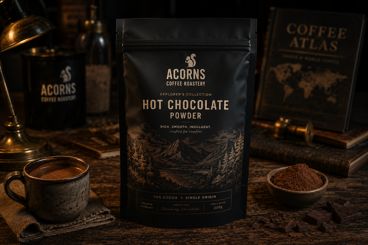 Acorns Coffee Roasters hot chocolate powder package on a wooden table with coffee-related items.
