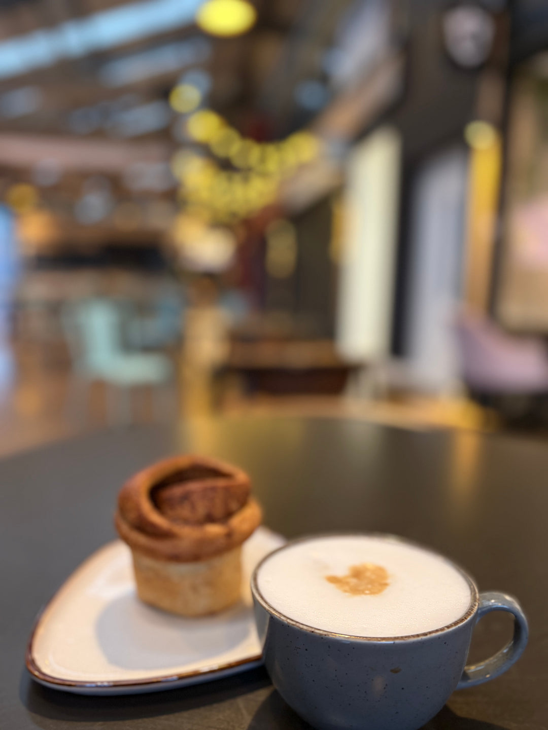 Cappuccino with a pastry on a table in a blurred cafe setting