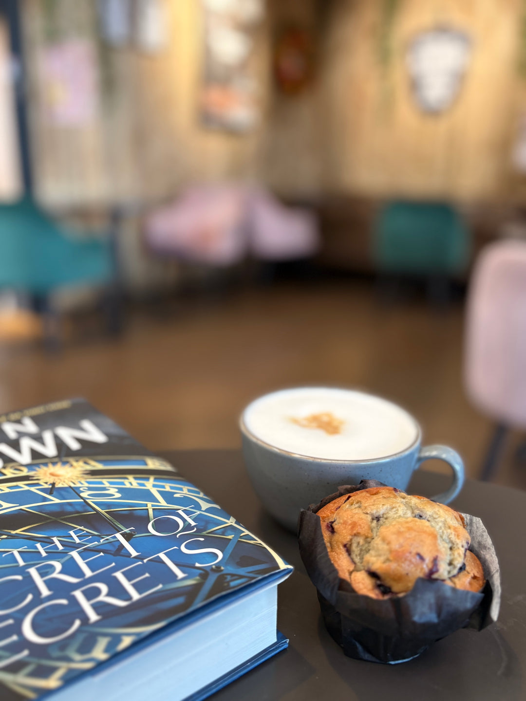 Cup of coffee and muffin on a table with books in a blurred cafe setting