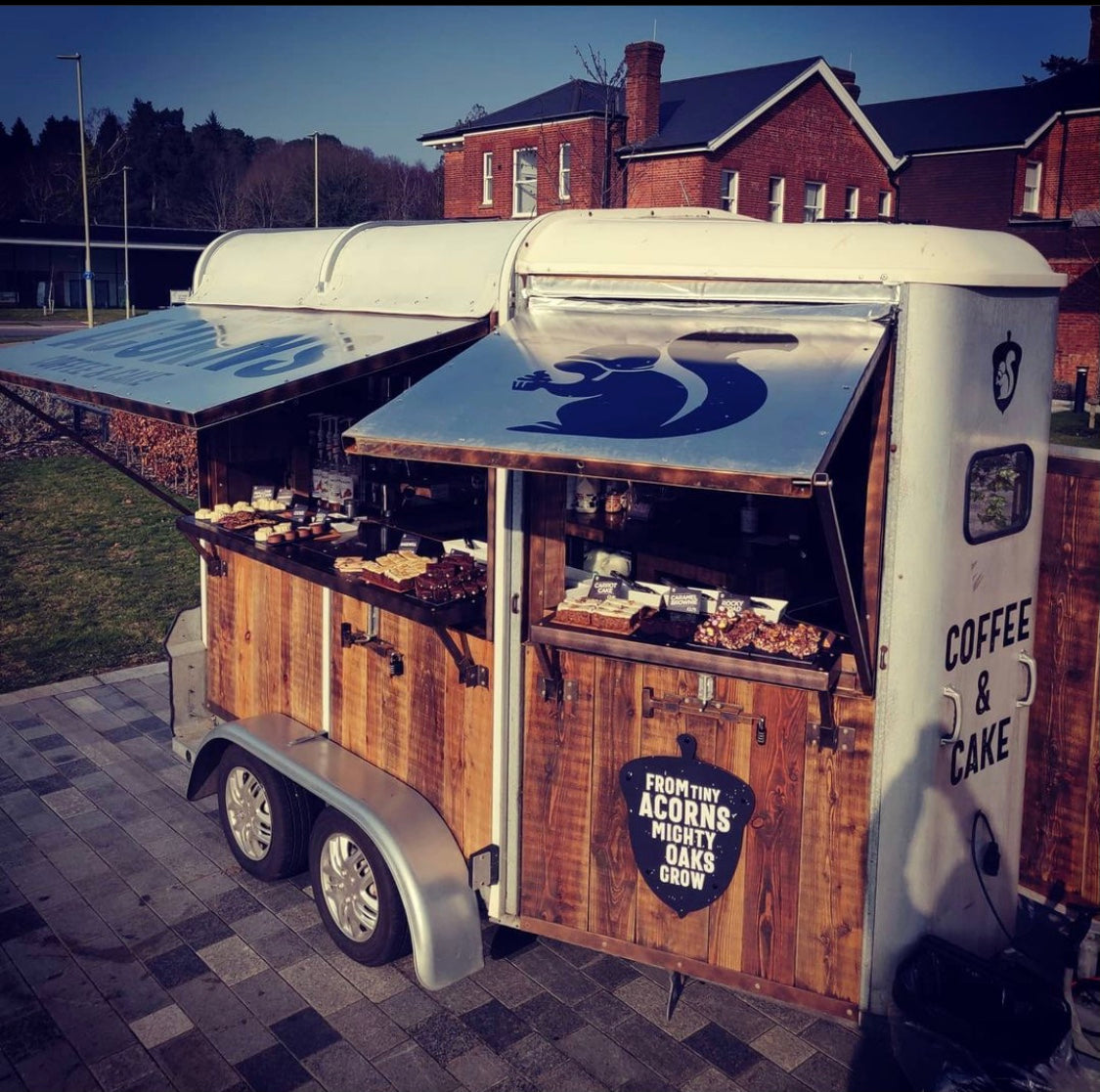 Wooden horsebox with 'Acorns Coffee & Cake' branding on a paved area.