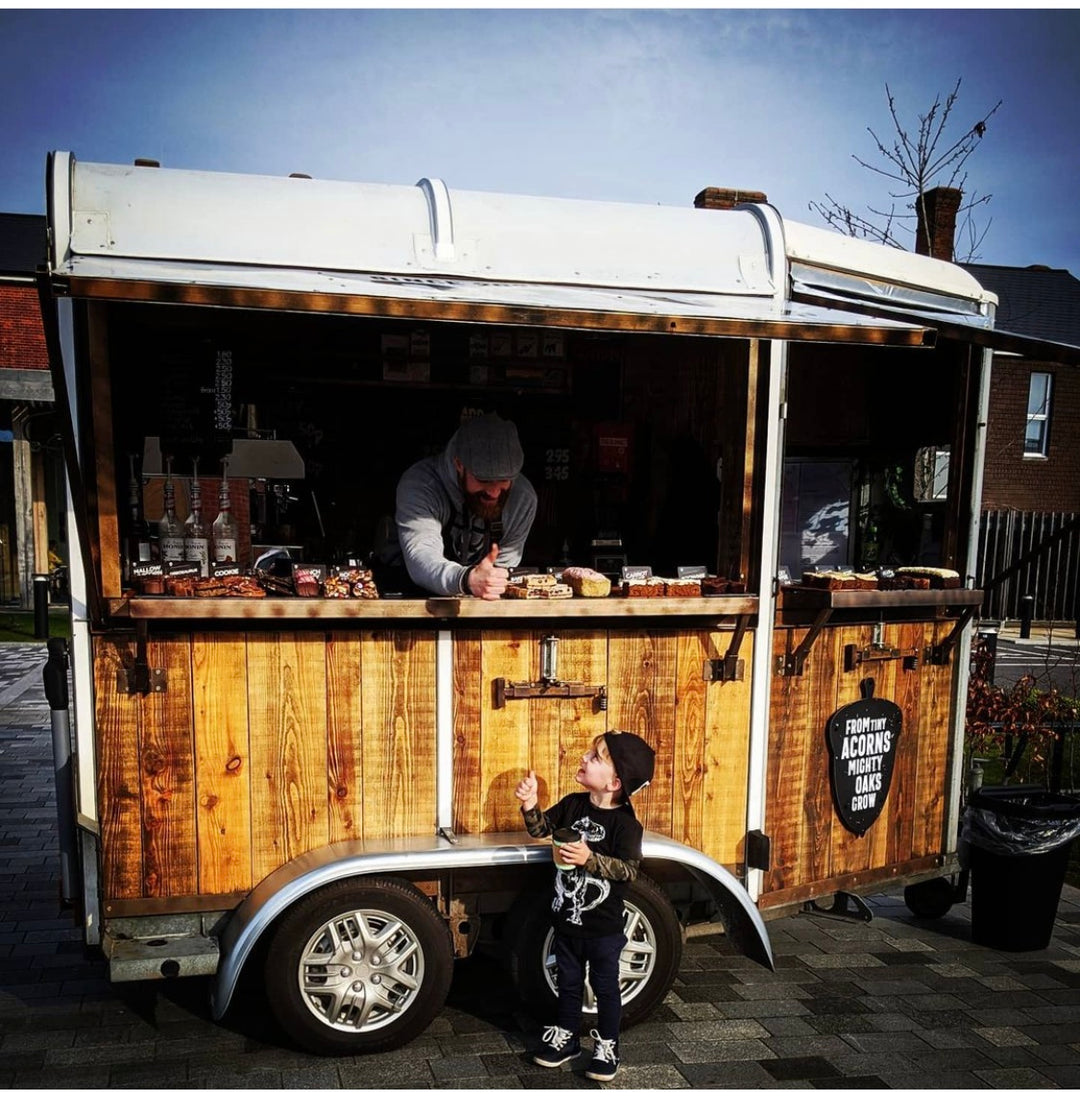 Wooden horsebox with a person and child interacting outdoors.